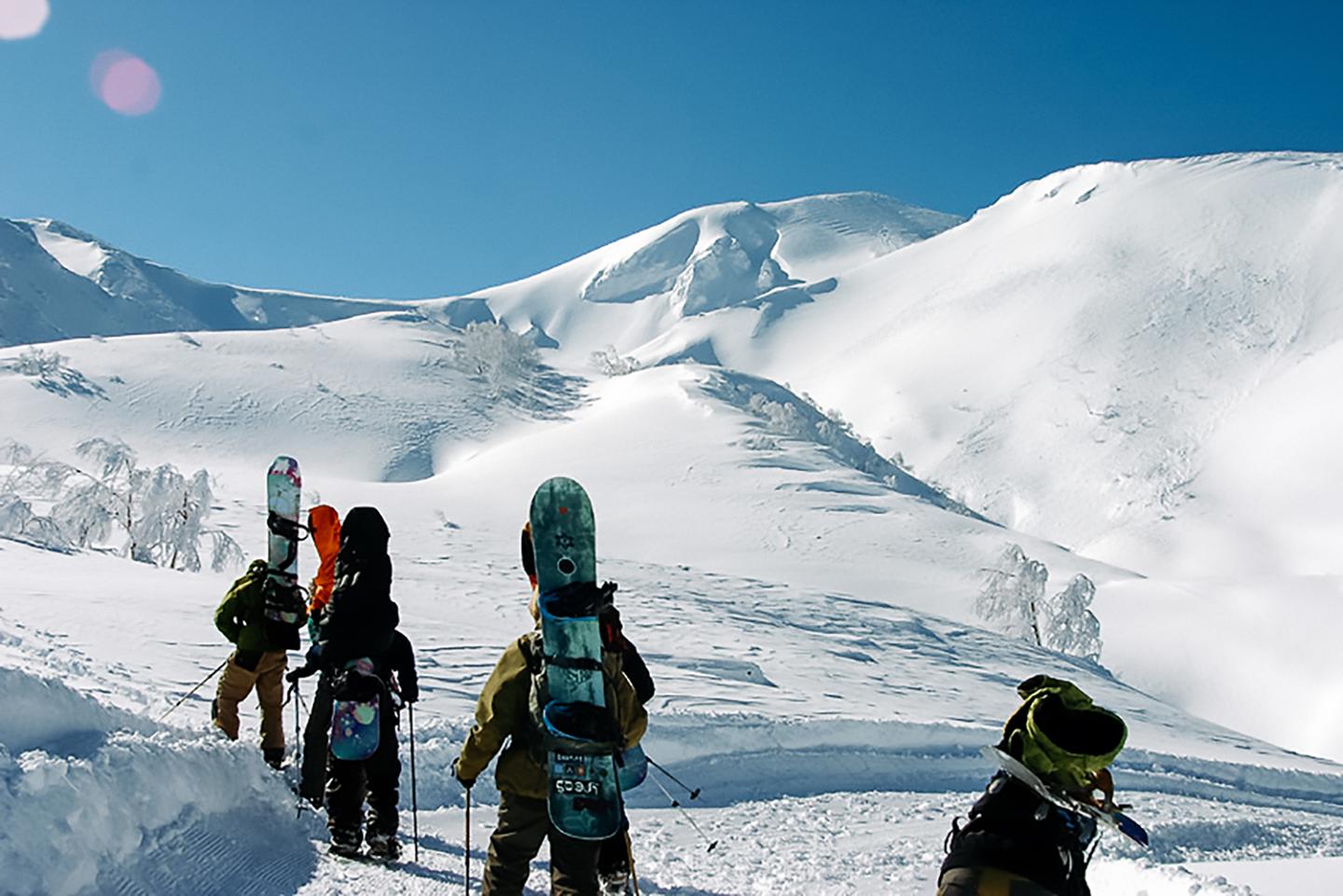 A group of snowboarders walking up a mountain