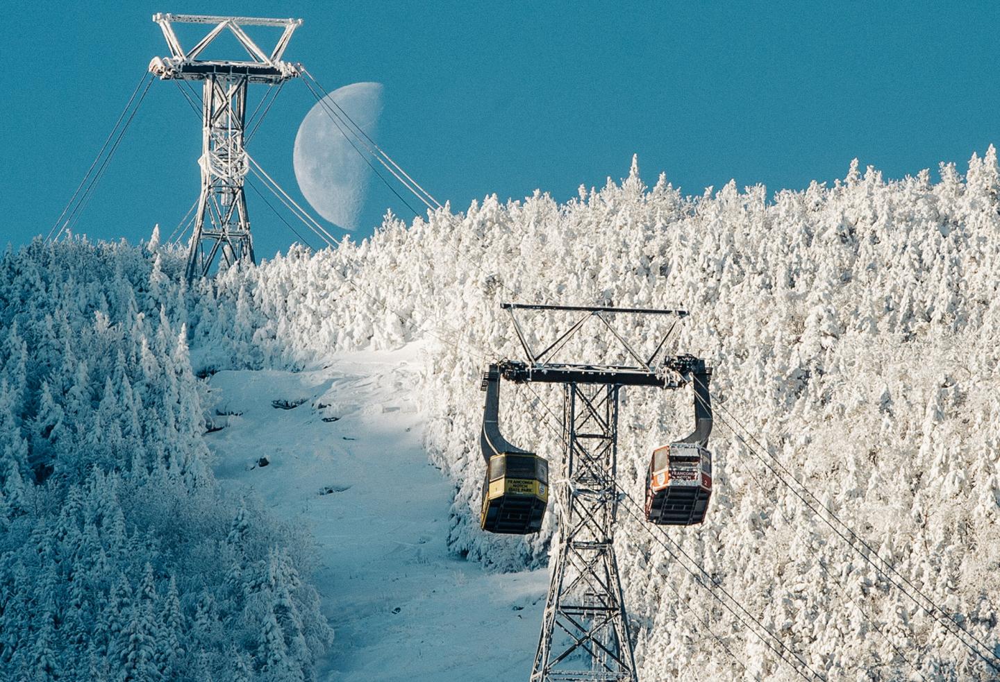 A close up of a gondola on a mountain with the moon in the sky