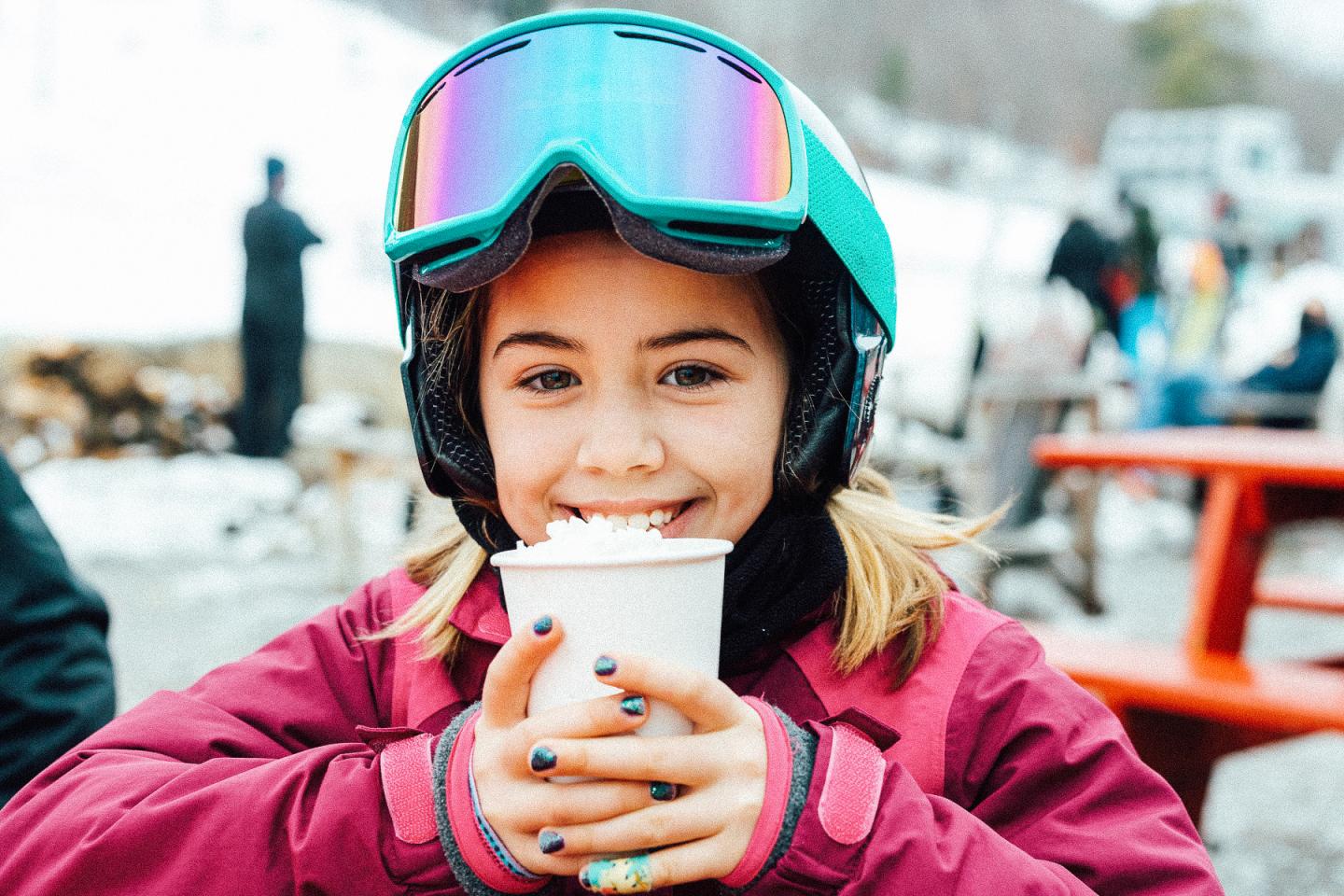A child in snow gear drinking a hot chocolate