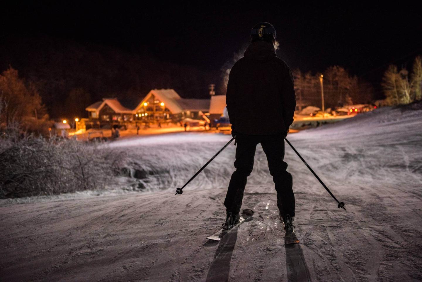 Camp Fortune skier in front of lodge at night