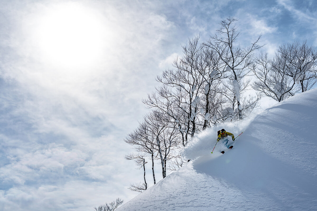 a skier in yellow on a ridge carving powder at Geto Kogen, Japan