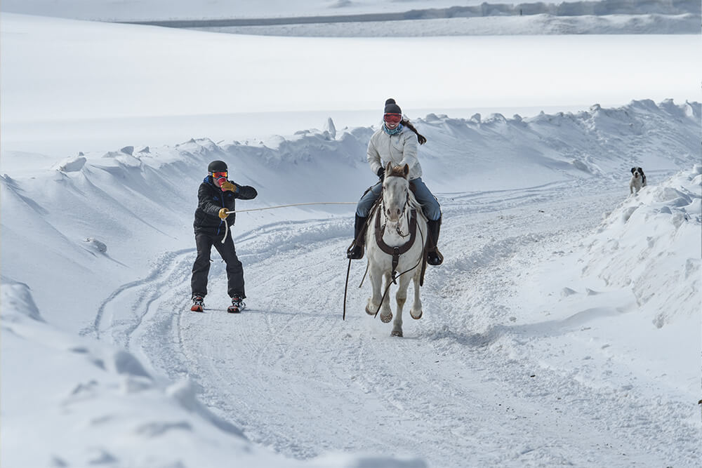 a skier chugging a beer being pulled by a woman on a horse at Antelope Butte, WY