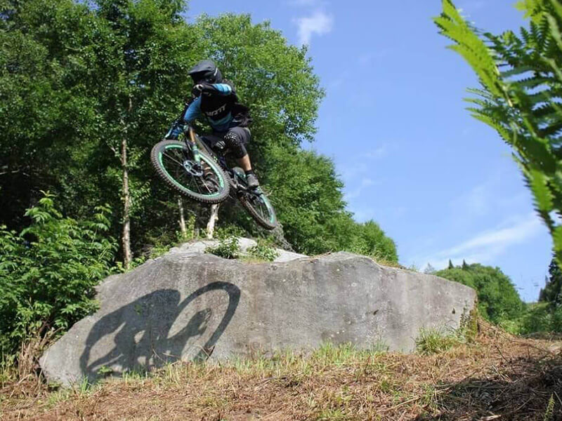 Bolton Valley VT biker jumping off a rock on a bike trail