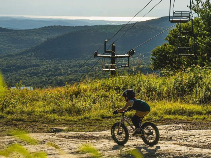 child mountain biking under a lift line at Bolton Valley, an Indy Pass Partner
