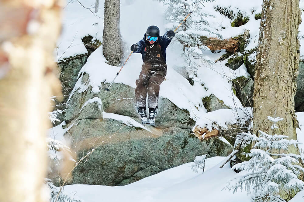 Skier jumping off a rock in the trees at Magic Mountain, VT